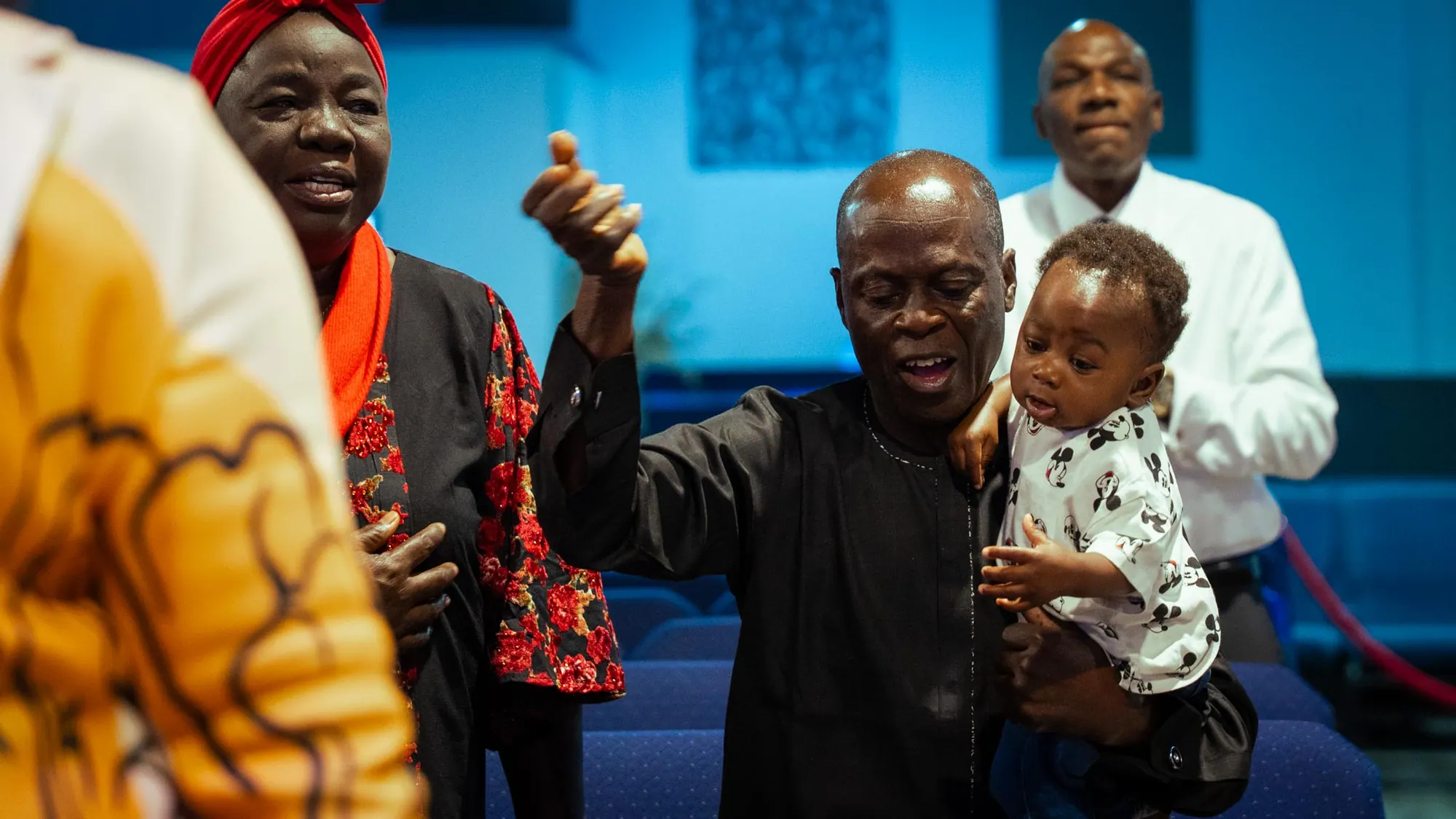 A man lifts a toddler high while singing in worship