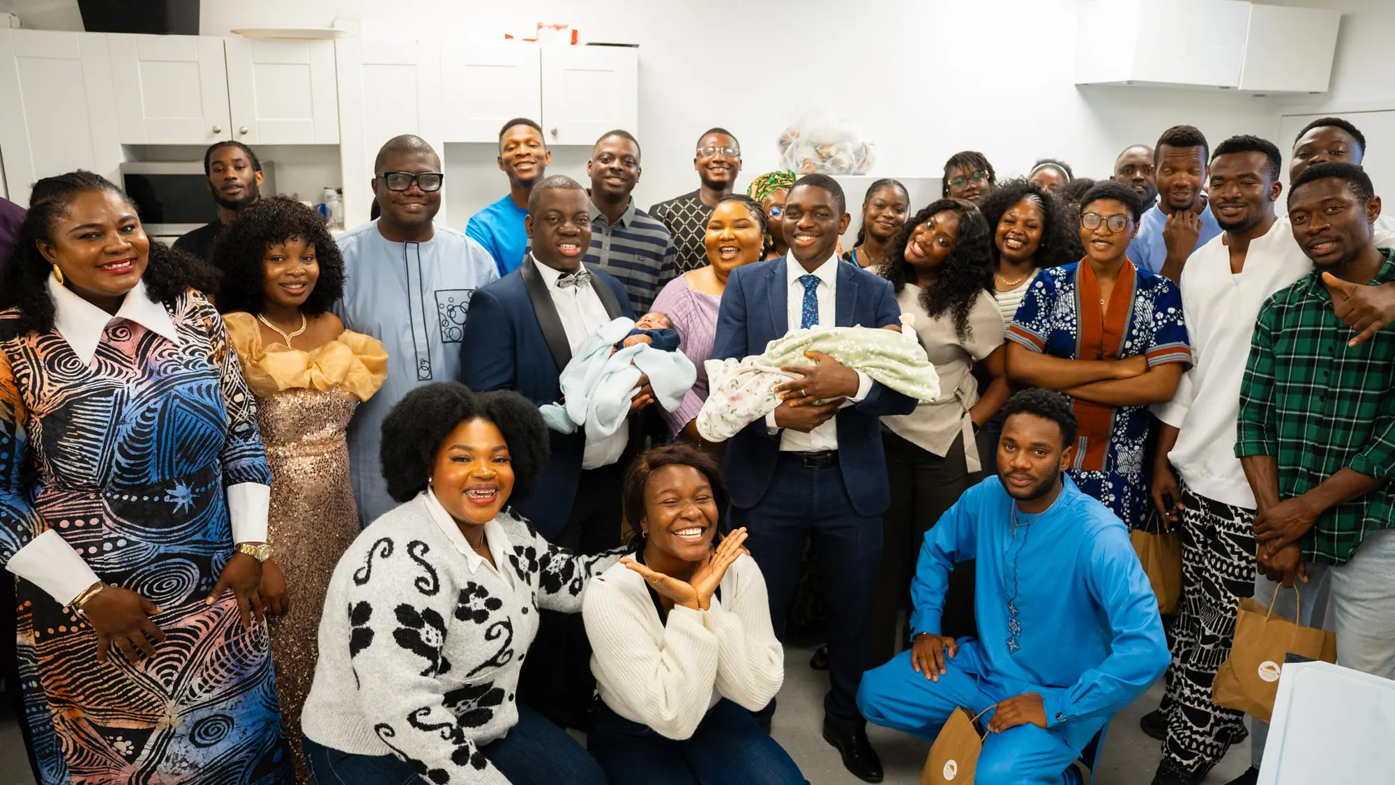 Friends and family crowd around two fathers holding their newborns after a dedication