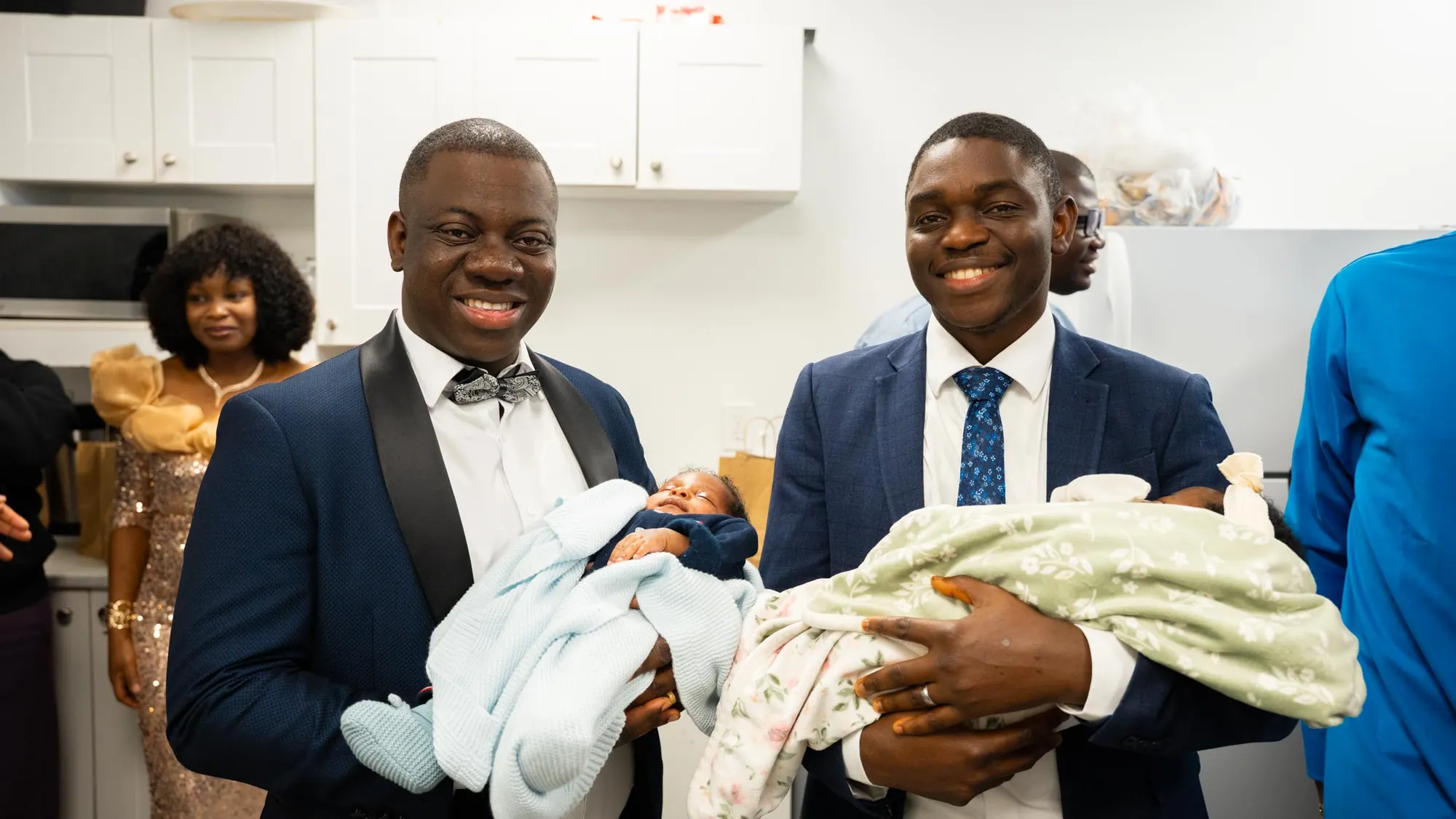 Two smiling fathers each hold a newborn at a child dedication